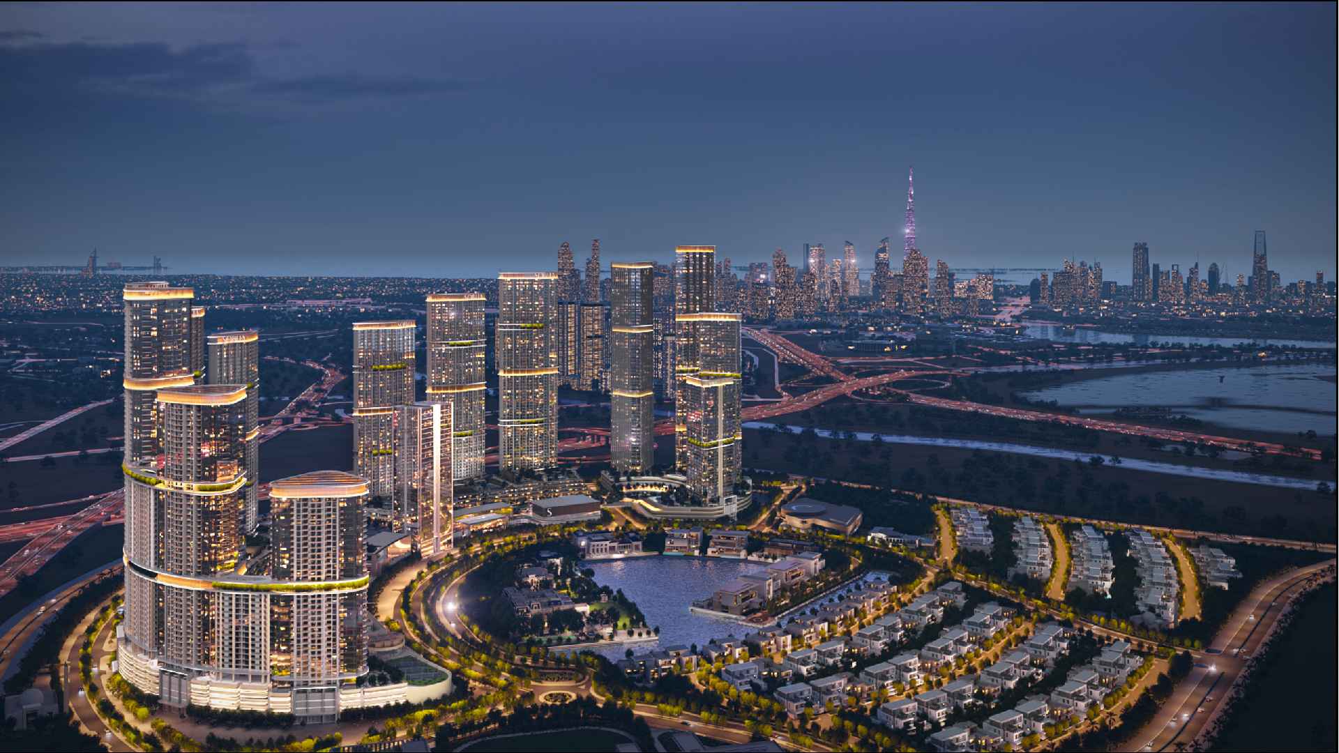Aerial night view of Sobha Realty master-planned waterfront community featuring illuminated high-rise towers, residential villas, landscaped roads, and Dubai skyline in the background