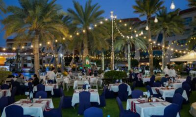 Outdoor Iftar dining setup at AL RAHA BEACH RESORT & SPA featuring beachfront tables under palm trees with warm string lights during evening.