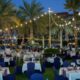 Outdoor Iftar dining setup at AL RAHA BEACH RESORT & SPA featuring beachfront tables under palm trees with warm string lights during evening.