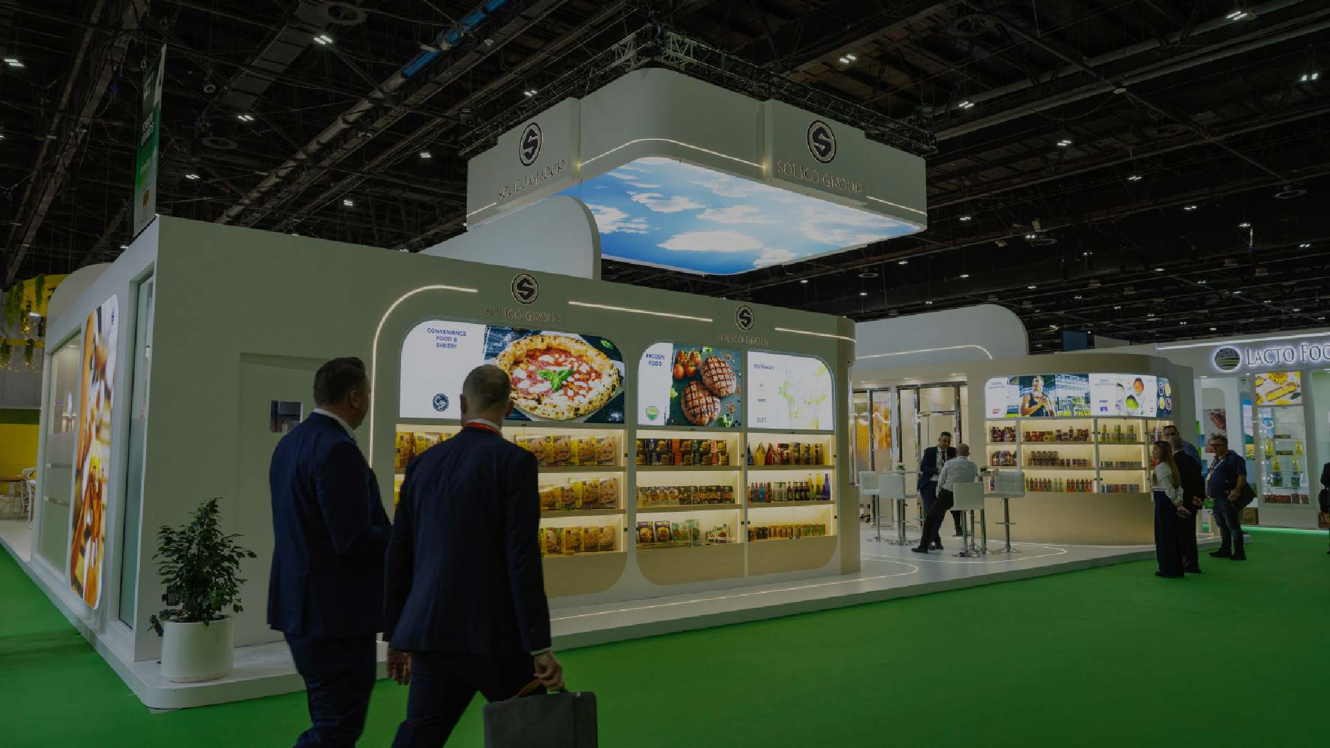 Solico Group exhibition stand at a trade show, featuring illuminated product displays while visitors walk and view food products.