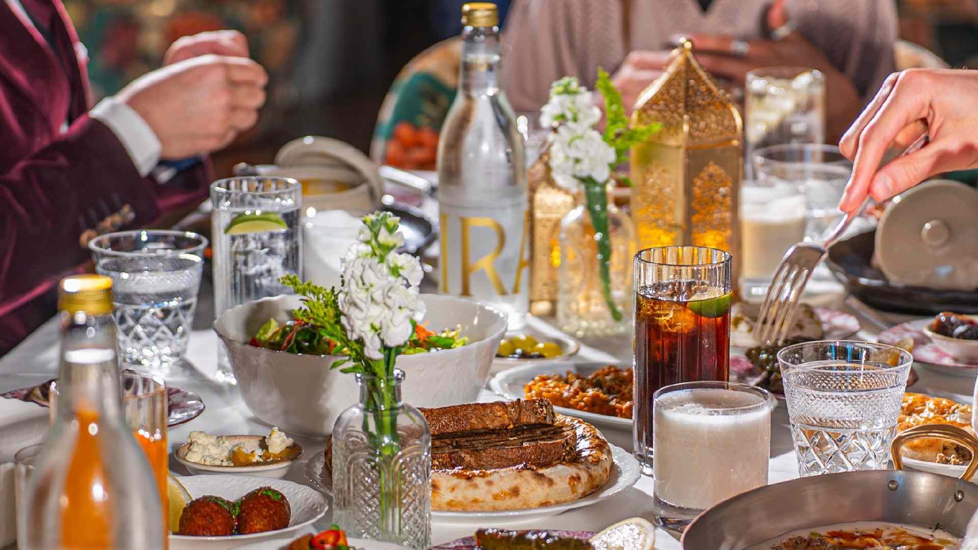 Shared Iftar table at Blume featuring Middle Eastern dishes, flatbreads, dips, dates, drinks, and lanterns as guests serve food together