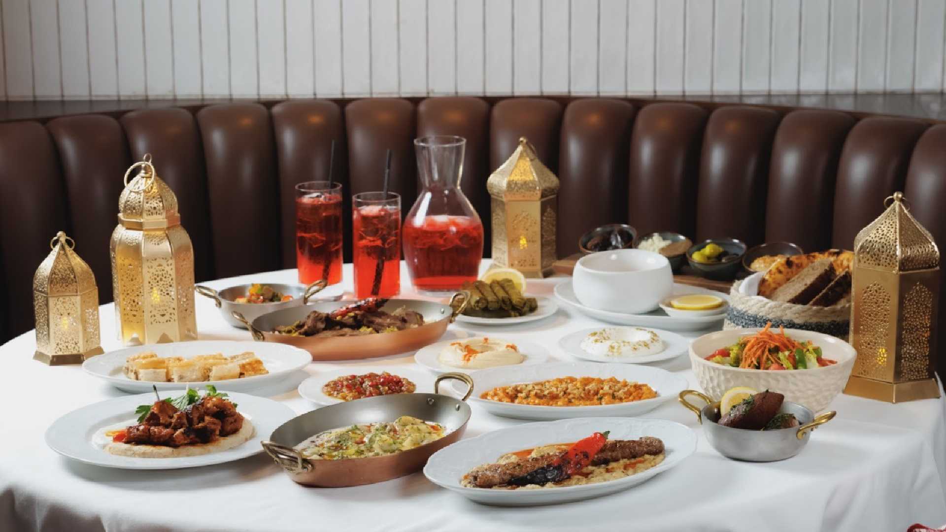 Ramadan Iftar table at FUMÉE STEAKHOUSE featuring shared mezze, grilled meats, soups, bread, desserts and traditional lanterns set on a white tablecloth.