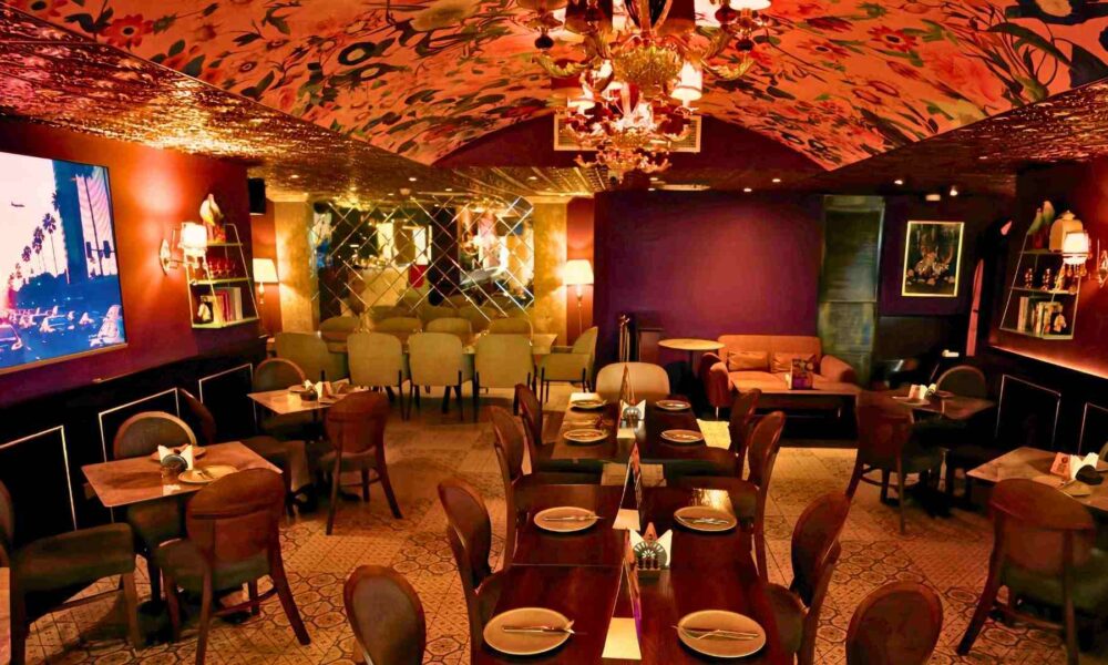 Warmly lit interior of The Permit Room restaurant featuring set dining tables, upholstered chairs, a patterned ceiling, and an intimate lounge-style ambience designed for group dining.