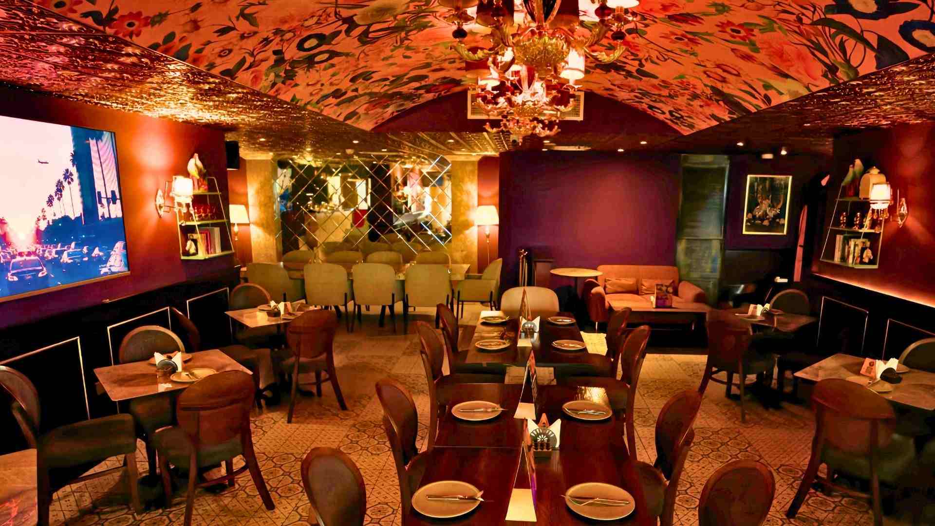 Warmly lit interior of The Permit Room restaurant featuring set dining tables, upholstered chairs, a patterned ceiling, and an intimate lounge-style ambience designed for group dining.