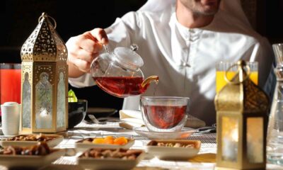 Man pours hot Arabic tea from glass teapot into a clear cup on a Ramadan table with lanterns and dates at Hilton Garden Inn Dubai.