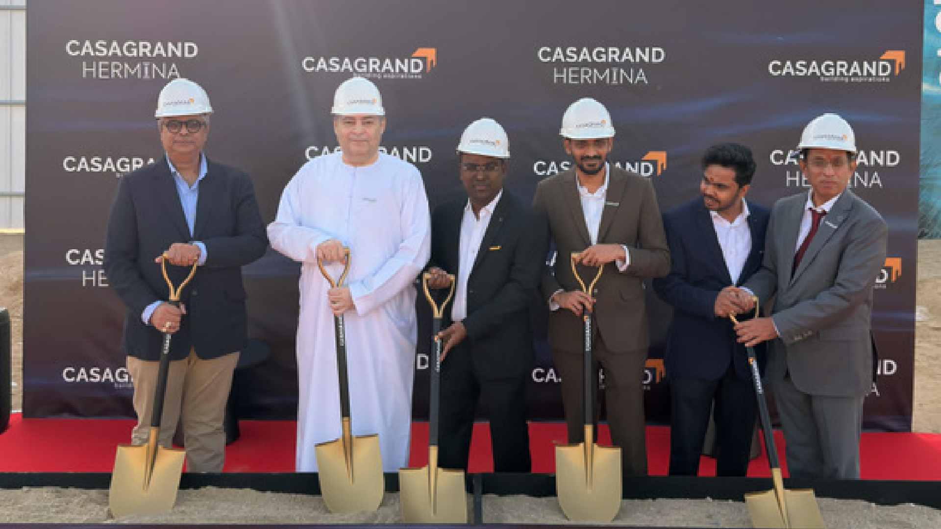 CASAGRAND HERMINA ground breaking ceremony with officials wearing safety helmets holding ceremonial shovels on a red carpet in front of CASAGRAND HERMINA branded backdrop