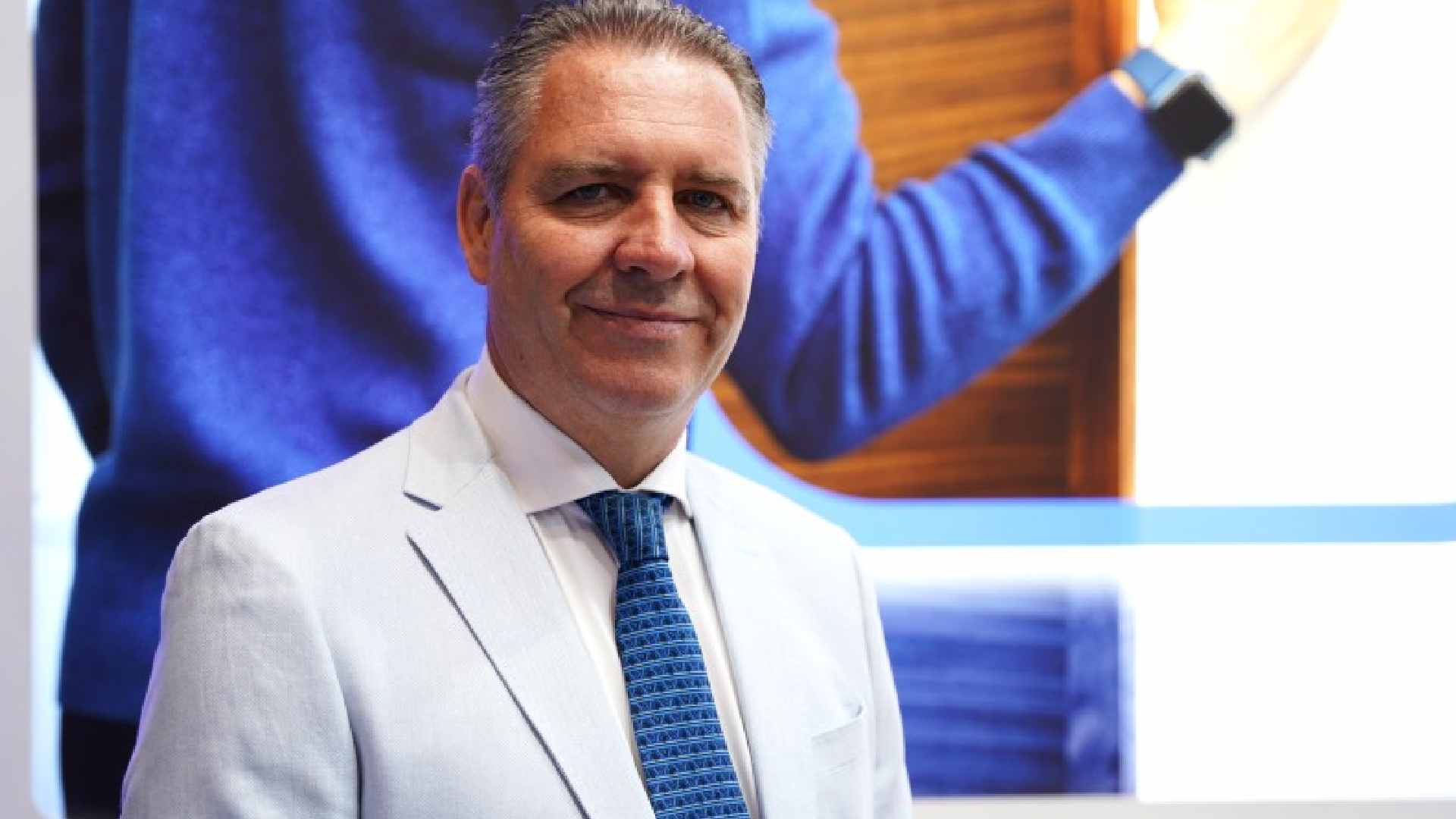 HID executive in a white suit and blue tie standing in front of a digital screen, presenting identity and access control solutions at an industry event.