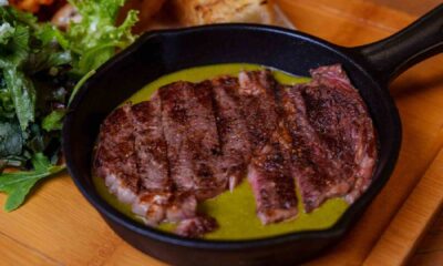 Grilled sliced steak served in a black cast iron skillet with green sauce, fries and fresh salad at Spartan Sports Bar
