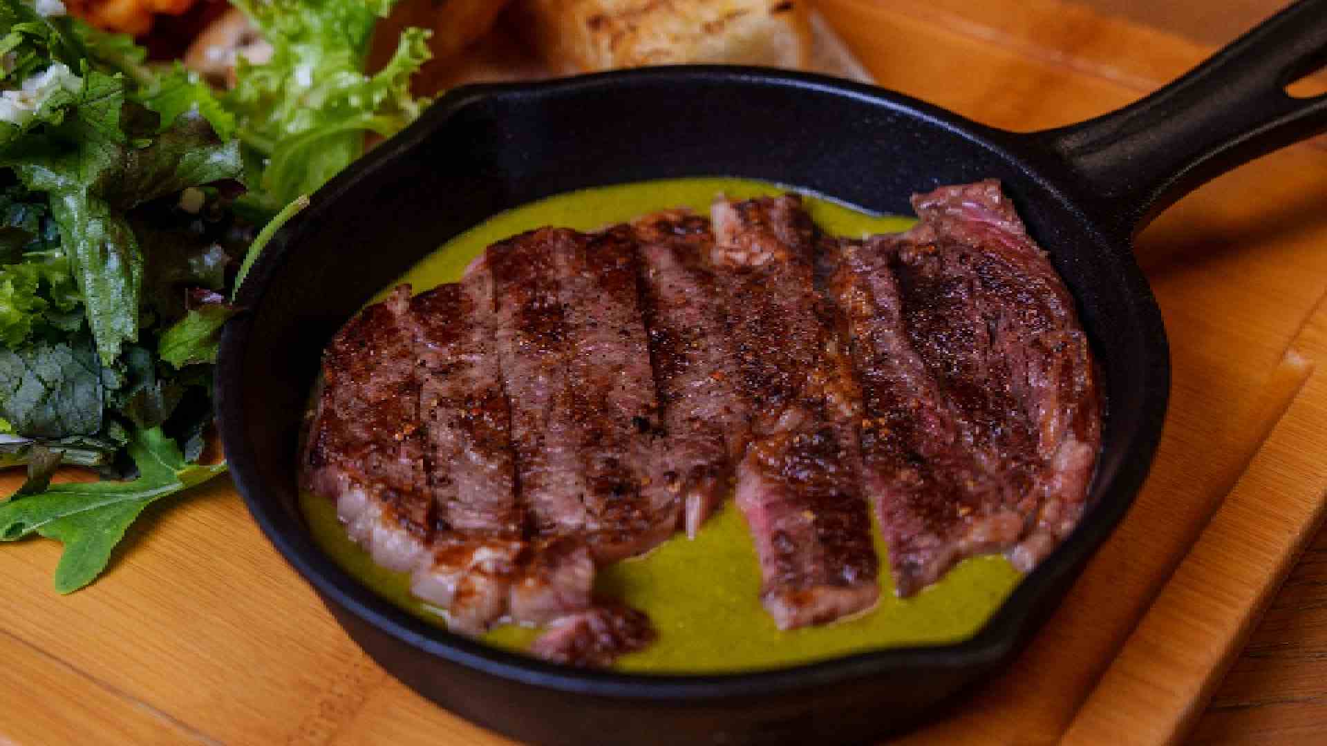 Grilled sliced steak served in a black cast iron skillet with green sauce, fries and fresh salad at Spartan Sports Bar