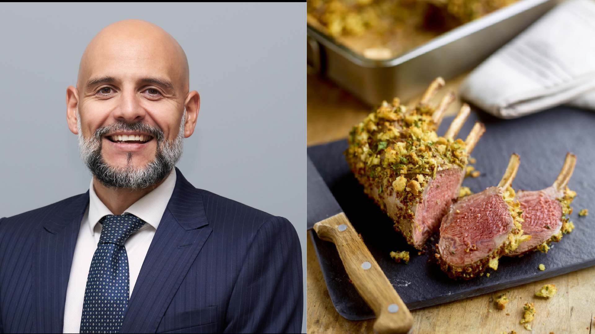 A man wearing a dark pinstripe suit, white shirt and navy tie standing for a professional portrait next to a sliced herb‑crusted rack of lamb served on a cutting board with a wooden‑handled knife.