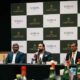 A Sobha Realty press conference panel with company representatives seated at a table, speaking into microphones, with Sobha Sanctuary and Sobha Realty branded backdrop behind them and water bottles arranged on the table.