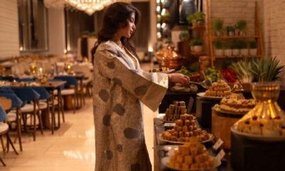 A woman in an elegant abaya serving herself from a beautifully arranged dessert buffet at Timo Restaurant, featuring trays of Middle Eastern sweets, warm lighting, and a refined dining area set for Ramadan