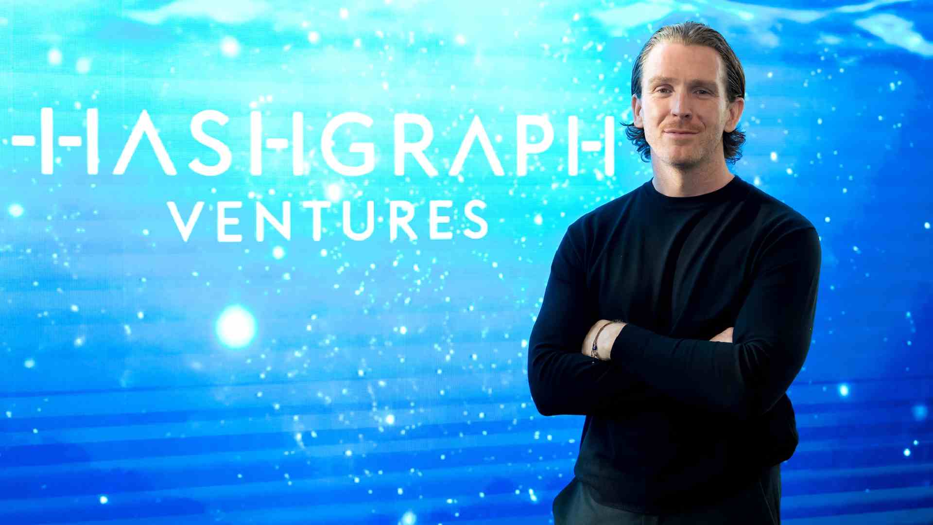 A person standing with arms crossed in front of a digital blue gradient background featuring the Hashgraph Ventures logo.