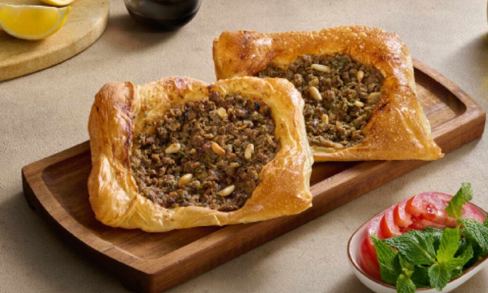 Open Lebanese lahme baajine pastries filled with spiced minced meat, served on a wooden board with lemon, olive oil and fresh salad at AL HALLAB.