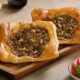 Open Lebanese lahme baajine pastries filled with spiced minced meat, served on a wooden board with lemon, olive oil and fresh salad at AL HALLAB.