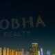 Drone show forming the words ‘Sobha Realty’ in illuminated lights above Dubai Marina skyline at night, with high-rise buildings and the Dubai Ferris wheel visible in the background.