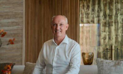 Guest seated in a Solenna Villas living area, wearing a white shirt, with wood-panelled walls, soft furnishings, and decorative glass accents in the background.