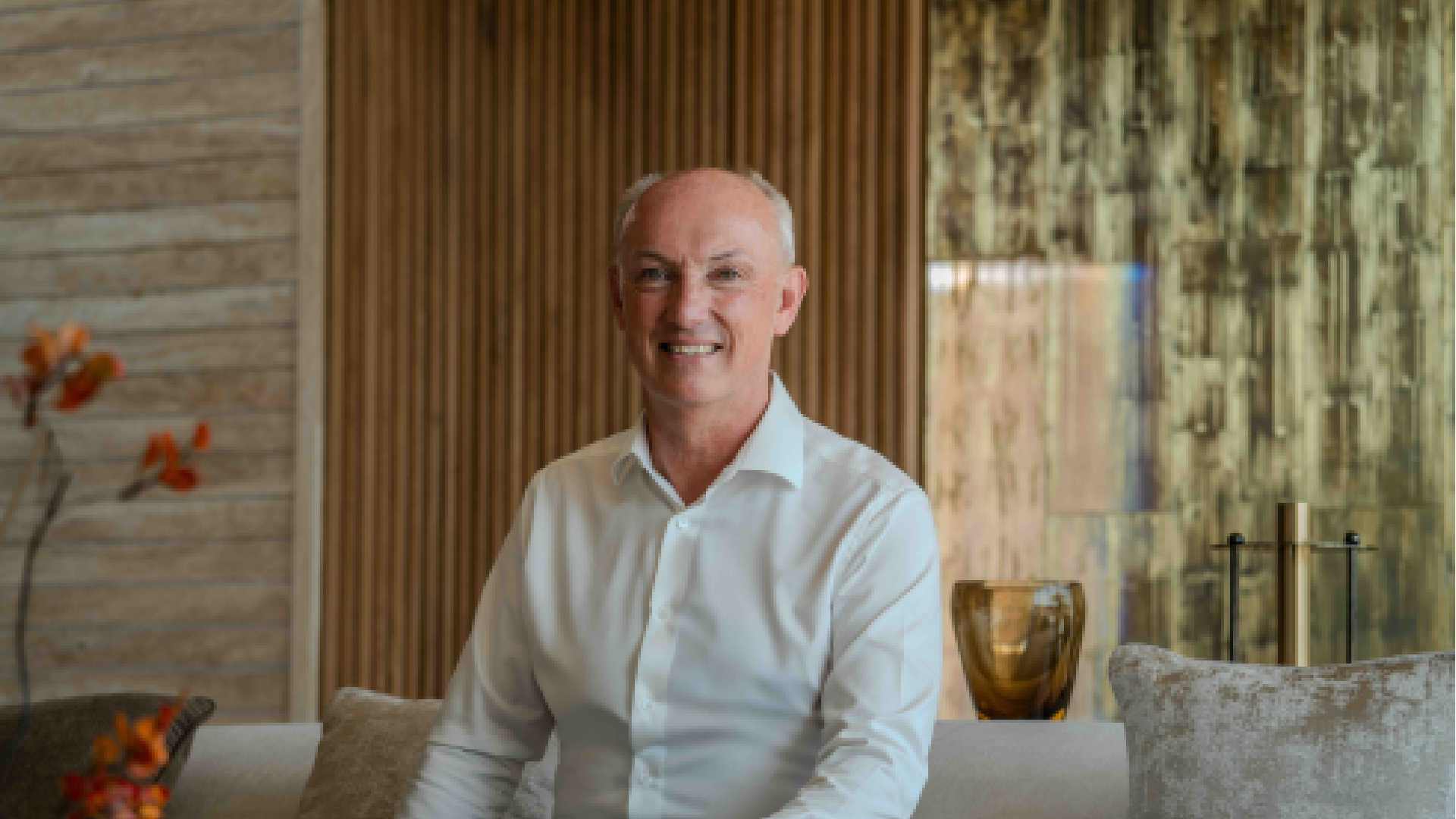 Guest seated in a Solenna Villas living area, wearing a white shirt, with wood-panelled walls, soft furnishings, and decorative glass accents in the background.