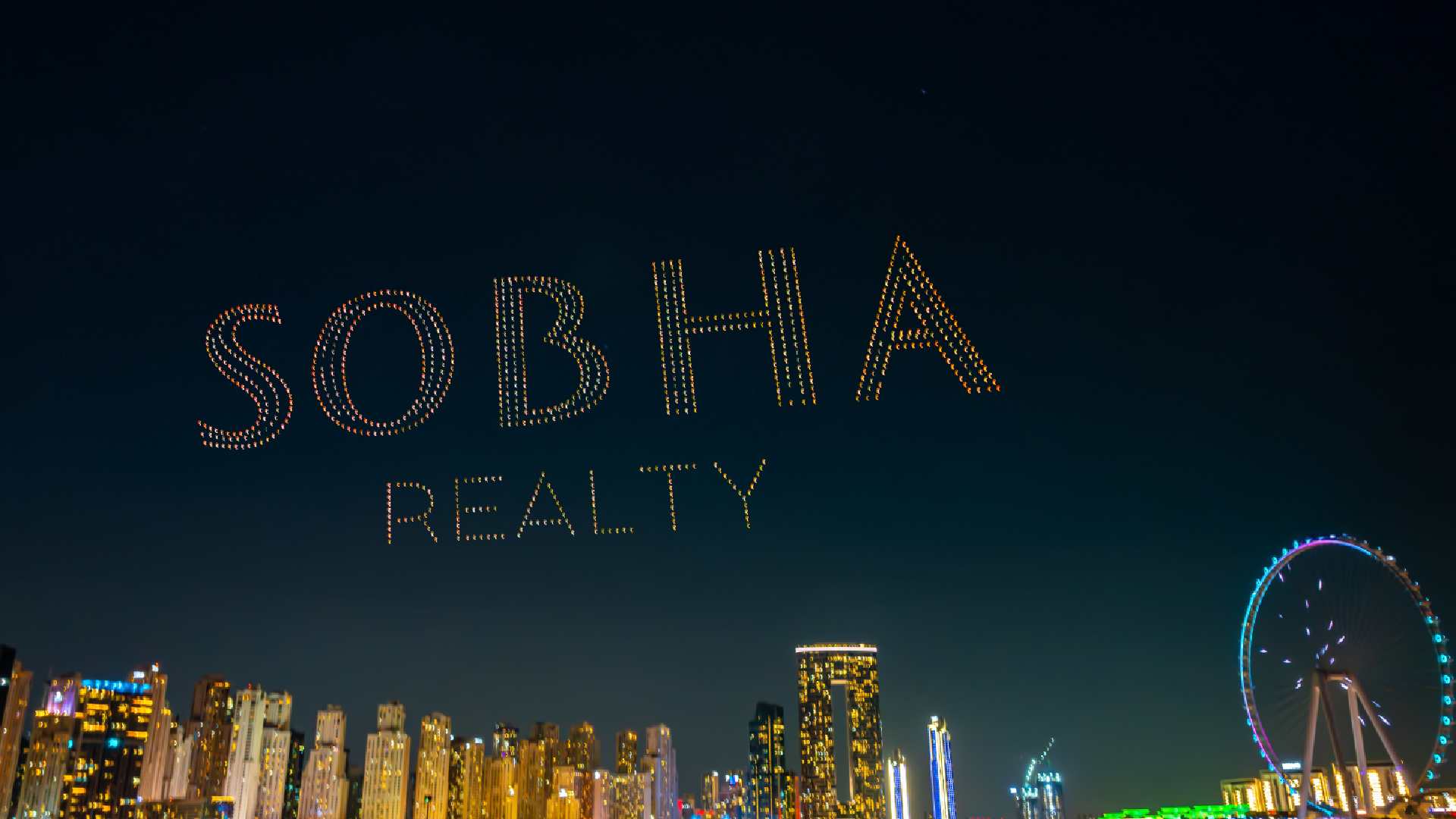 Drone show forming the words ‘Sobha Realty’ in illuminated lights above Dubai Marina skyline at night, with high-rise buildings and the Dubai Ferris wheel visible in the background.