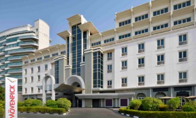 Exterior view of MÖVENPICK HOTEL APARTMENTS Bur Dubai showing the main entrance, white facade, arched driveway, and landscaped front area under clear daylight
