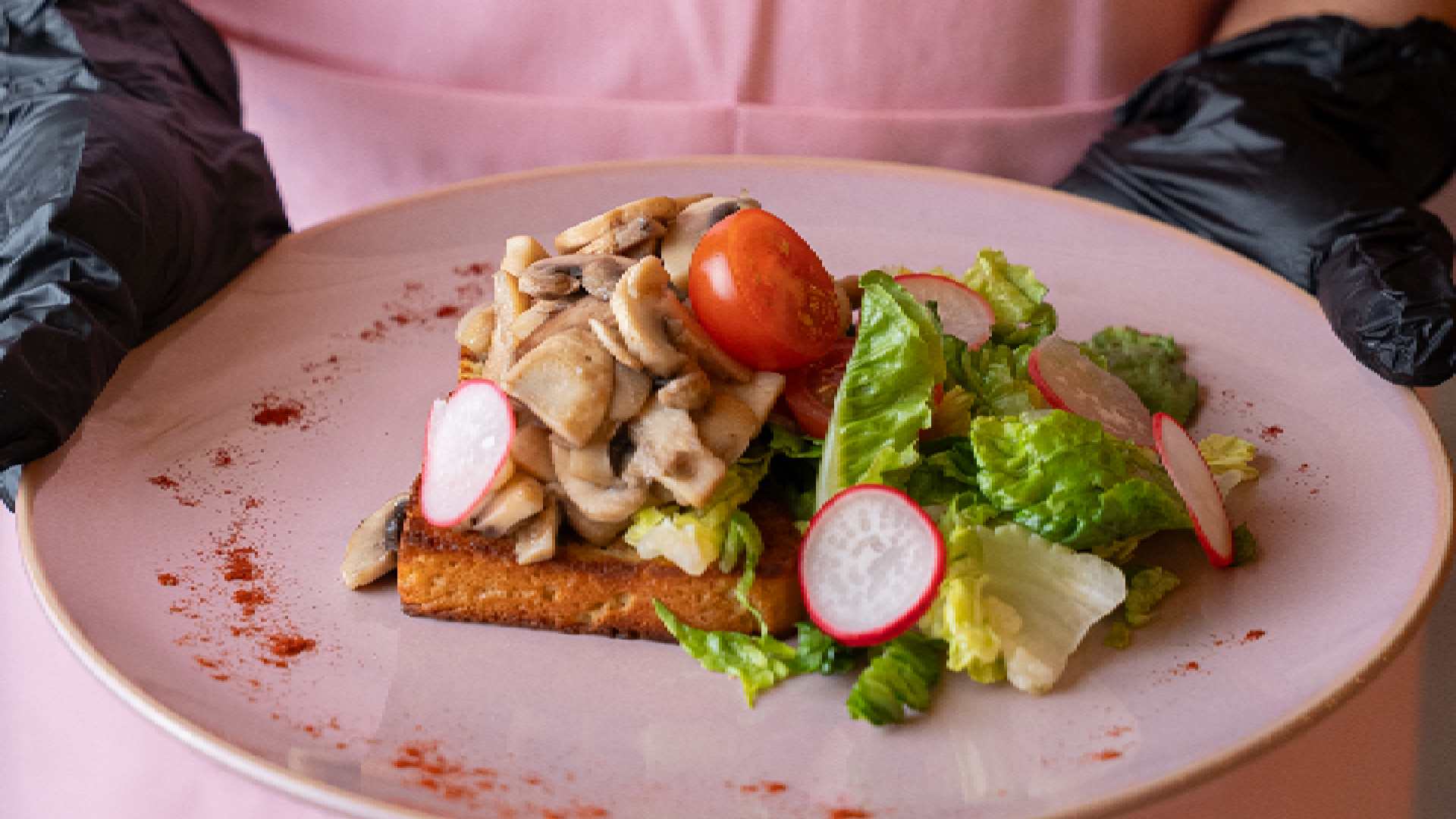 Split image showing Hola Zero Sugar Cafe branding: on the left, a server wearing a Hola Zero apron holding a plated keto dish with vegetables; on the right, the pastel pink Hola Zero Sugar Cafe seating area with diners under decorative floral lighting. ``