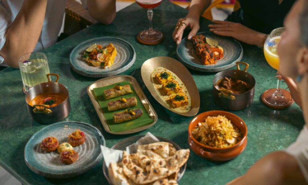 Overhead view of guests sharing assorted Indian dishes at Viceroy’s Table, including kebabs, curries, biryani, flatbreads, and plated starters on a green dining table.