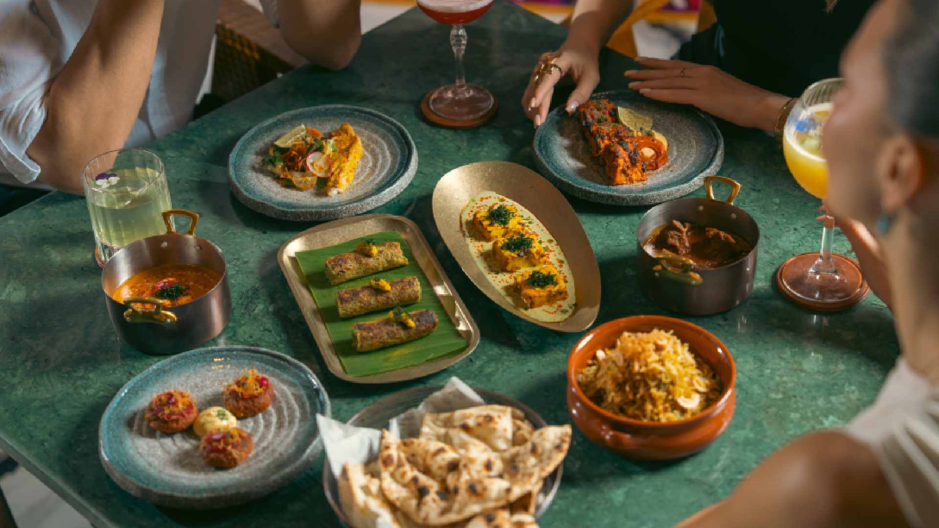 Overhead view of guests sharing assorted Indian dishes at Viceroy’s Table, including kebabs, curries, biryani, flatbreads, and plated starters on a green dining table.