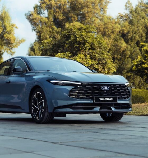 A three-quarter front view of a slate blue Ford Taurus sedan parked on a grey tiled courtyard.