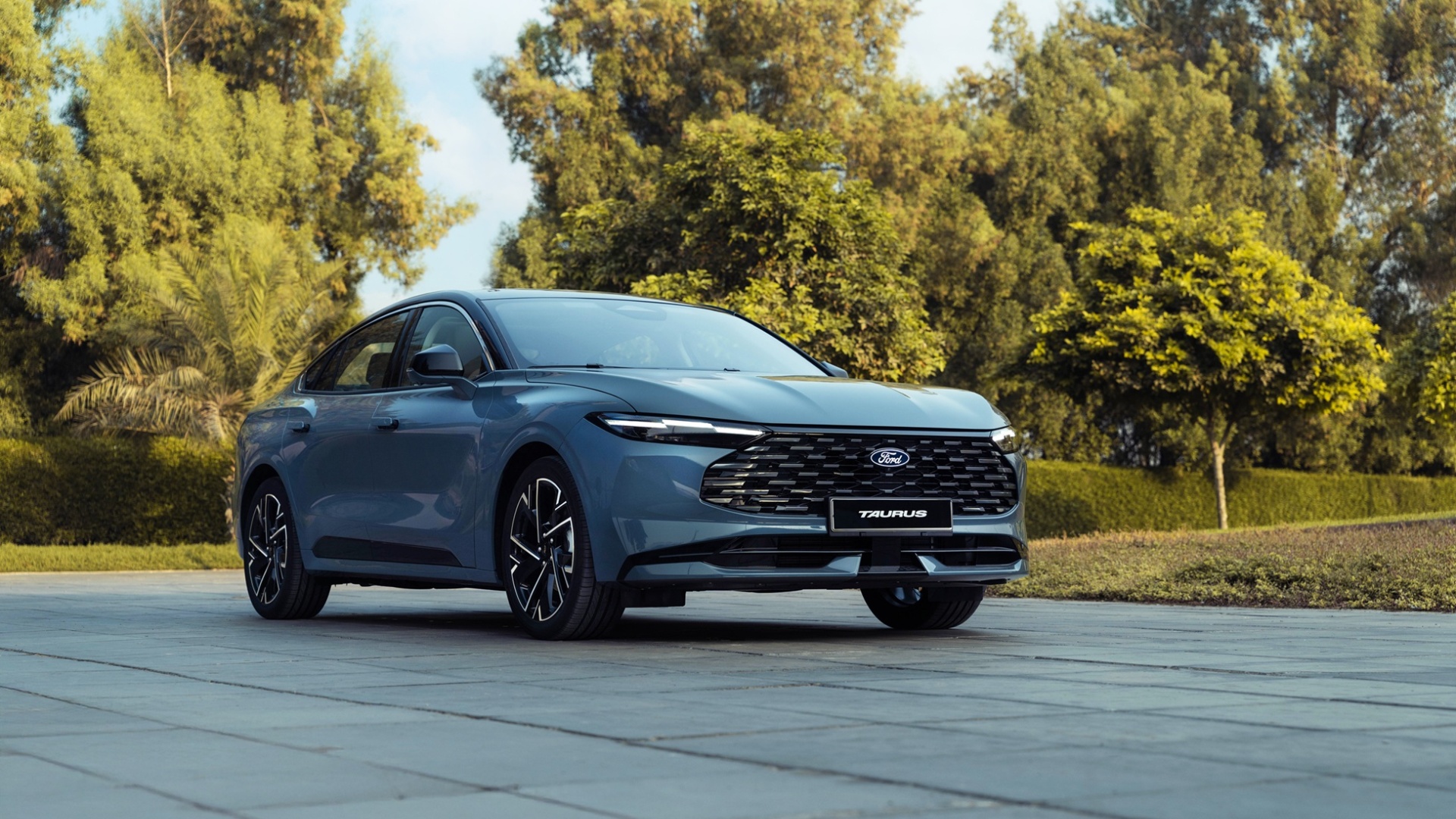 A three-quarter front view of a slate blue Ford Taurus sedan parked on a grey tiled courtyard.
