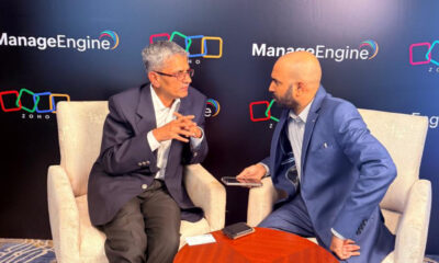 Shailesh Davey, Co-founder and CEO of Zoho, is seated in a cream-colored armchair and speaking with Srijith KN, Senior Editor at Integrator Media, who is holding a recording device. They are positioned in front of a dark backdrop featuring the ManageEngine and Zoho logos during a professional interview.