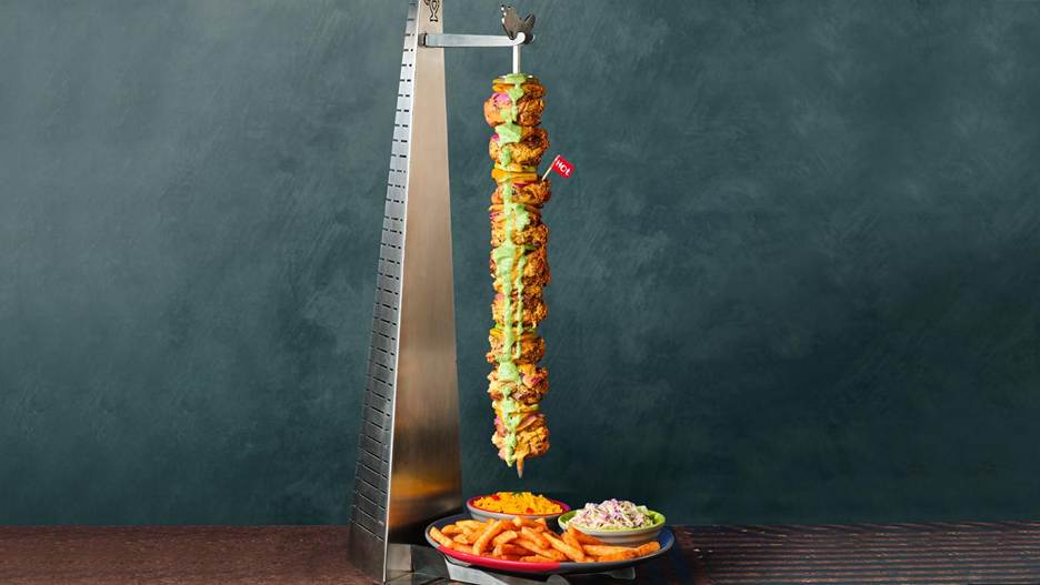 Nando’s UAE Espetada A Torre with stacked PERi‑PERi chicken thighs, peppers, onions and lime slices hanging vertically over a table, served with sides.