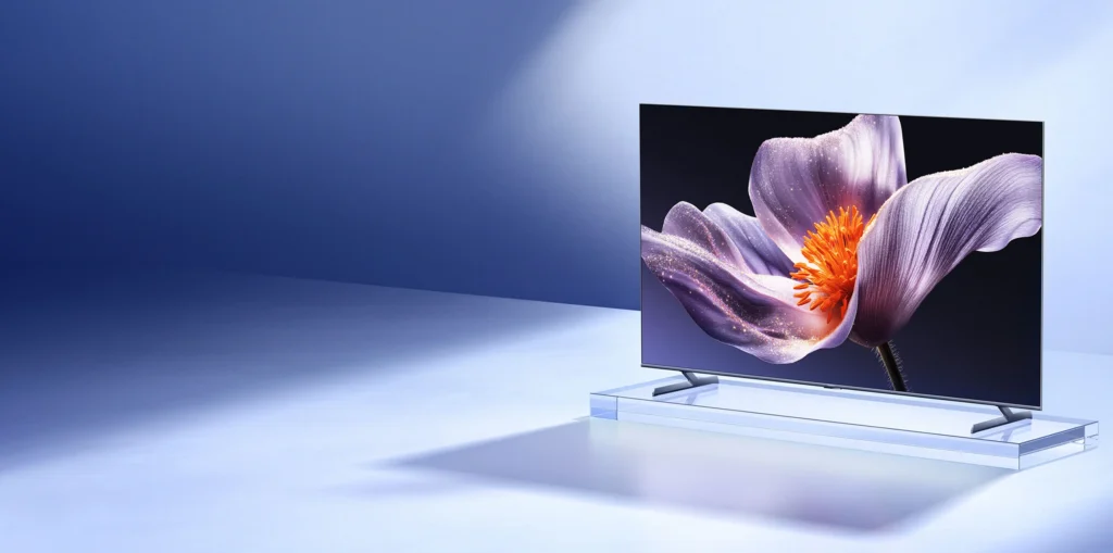The Xiaomi TV S Pro Mini LED 2026 displayed with a vibrant purple flower on its ultra-slim, bezel-less screen. The image showcases the TV's high dynamic range and deep contrast, emphasizing its QLED quantum dot technology and metallic unibody design.