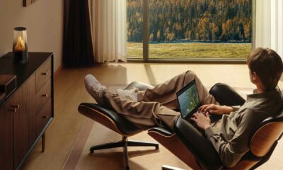 Person relaxing in a modern living room, using a tablet while the HUAWEI WiFi Mesh X3 Pro router glows on a sideboard near a large window overlooking sunlit mountains.