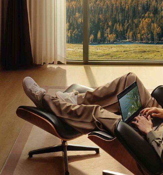 Person relaxing in a modern living room, using a tablet while the HUAWEI WiFi Mesh X3 Pro router glows on a sideboard near a large window overlooking sunlit mountains.