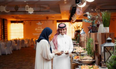 A Ramadan Iftar buffet setup at a Radisson Blu venue, featuring two guests selecting food from an elegantly arranged spread with traditional décor, warm lighting, and crescent moon ornaments overhead.