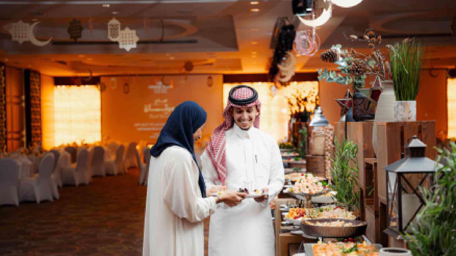 A Ramadan Iftar buffet setup at a Radisson Blu venue, featuring two guests selecting food from an elegantly arranged spread with traditional décor, warm lighting, and crescent moon ornaments overhead.