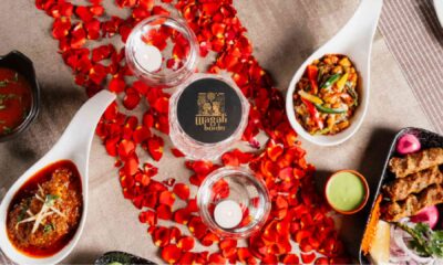 Overhead view of a romantic dining setup at Wagah Border featuring Indian dishes, kebabs, curries, candles, and red rose petals arranged on a table.