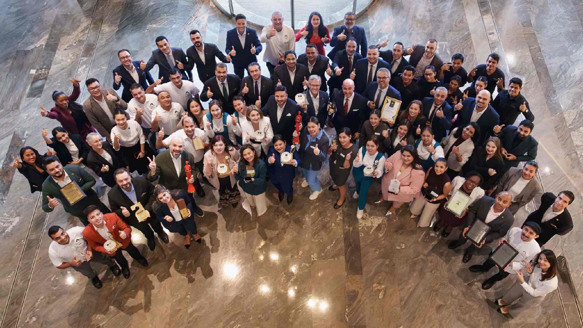 DAMAC Hospitality earns over 30 awards recognising excellence in luxury hospitality, leadership and guest experience. Group of DAMAC Hospitality team members standing together in a marble-floored atrium, holding multiple industry awards and trophies while posing for a celebratory group photo.