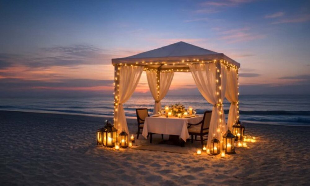 Private candlelit beachfront dining setup at Al Raha Beach Resort & Spa, featuring a draped gazebo with fairy lights, a table set for two, and lanterns on the sand at sunset overlooking the sea.