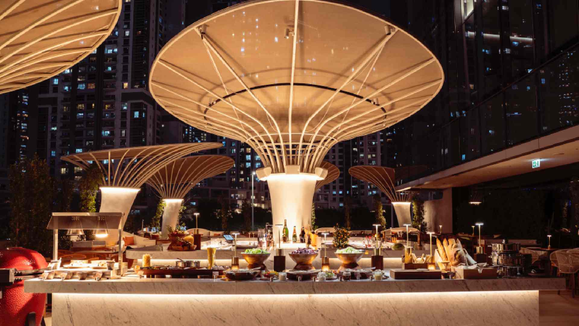 Open-air iftar buffet setup on the Pool Terrace at ME by Meliá Dubai, featuring illuminated food stations beneath sculptural canopy structures at night with the city skyline in the background.