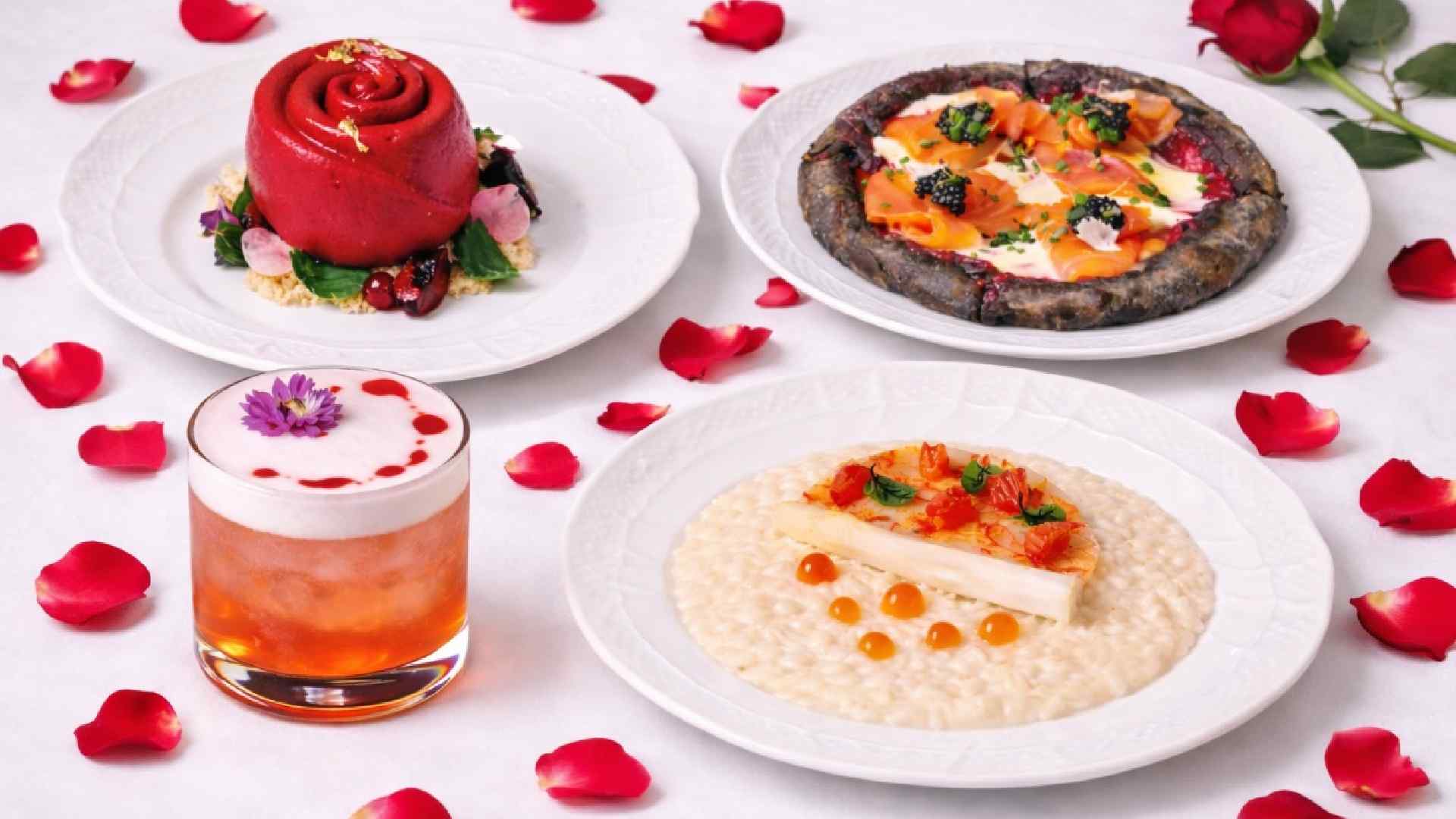 Artisan Valentine’s Day dining spread featuring dark chocolate rose dessert, salmon pizzetta with caviar, white asparagus risotto, and a cocktail, styled on a white table with scattered red rose petals