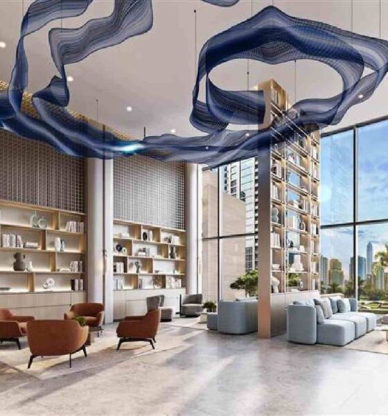 Double-height modern lobby interior by Opaal Interiors featuring floor-to-ceiling windows, sculptural blue suspended ceiling installation, built-in shelving, lounge seating, and city views beyond.