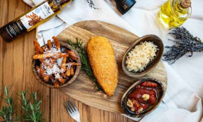 Top‑down view of a plated breaded fried cutlet with rosemary, sweet potato fries, sauerkraut, roast tomatoes, olive oil and seasonings on a wooden table at ME by Meliá Dubai