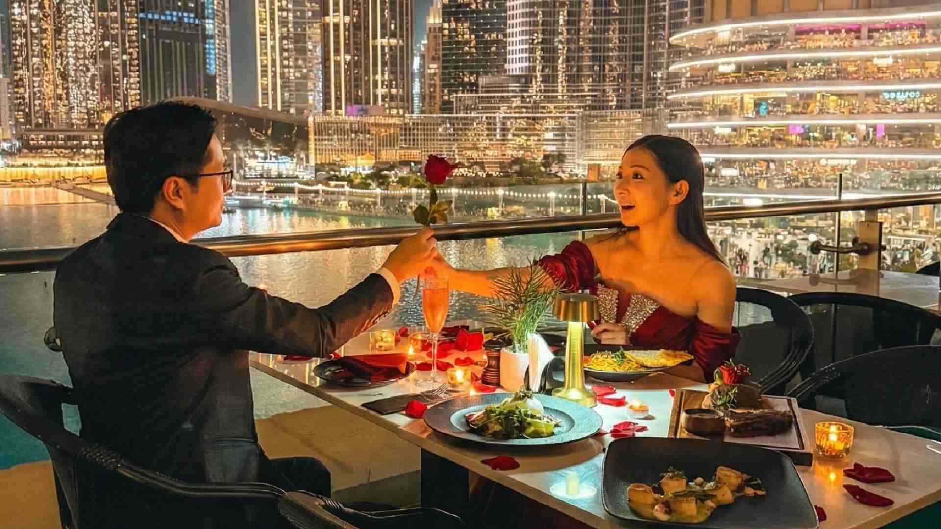 Romantic outdoor dinner at Joe’s Café Dubai with a couple dining by candlelight, exchanging a rose at a table overlooking the Burj Khalifa, Dubai Fountain, and illuminated city skyline at night.