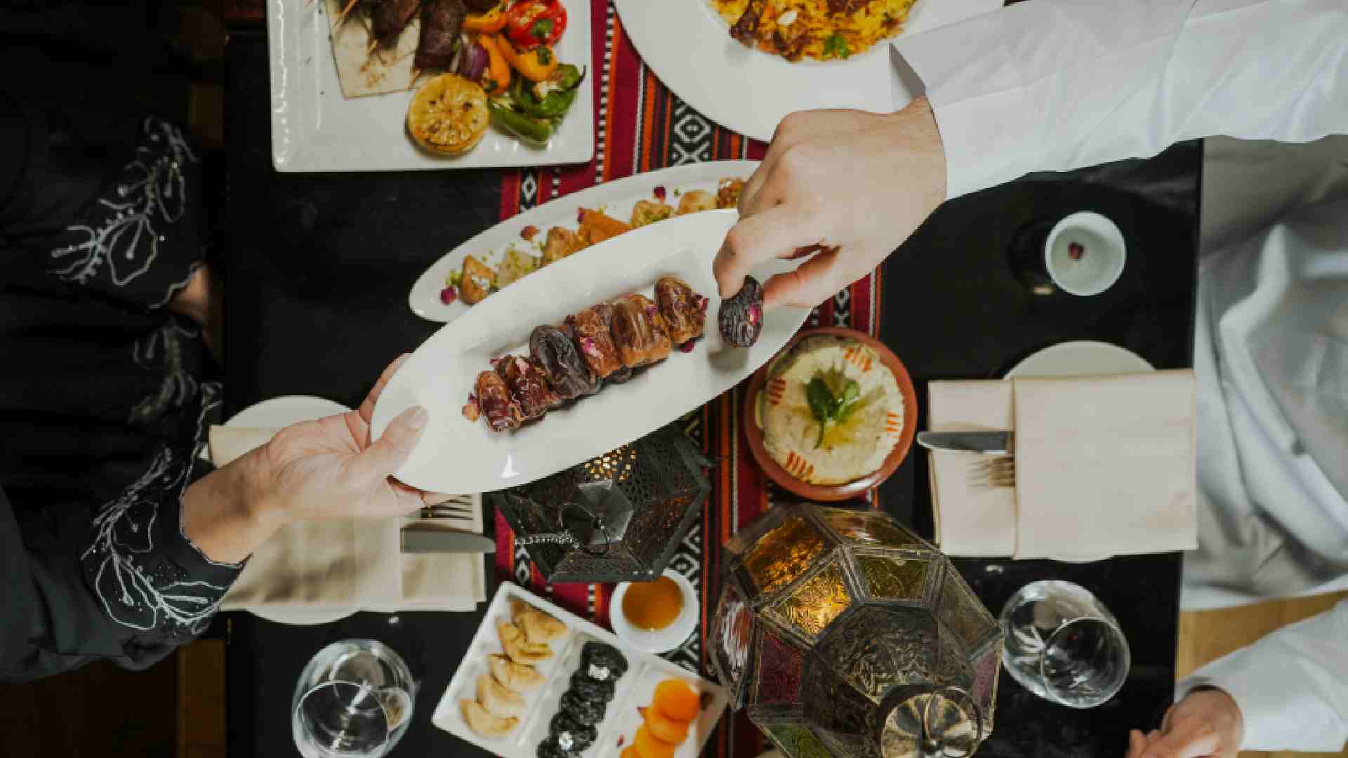 Overhead view of guests sharing a grilled meat platter with dates and Arabic dishes on a table at PARK REGIS KRIS KIN HOTEL DUBAI during Iftar.