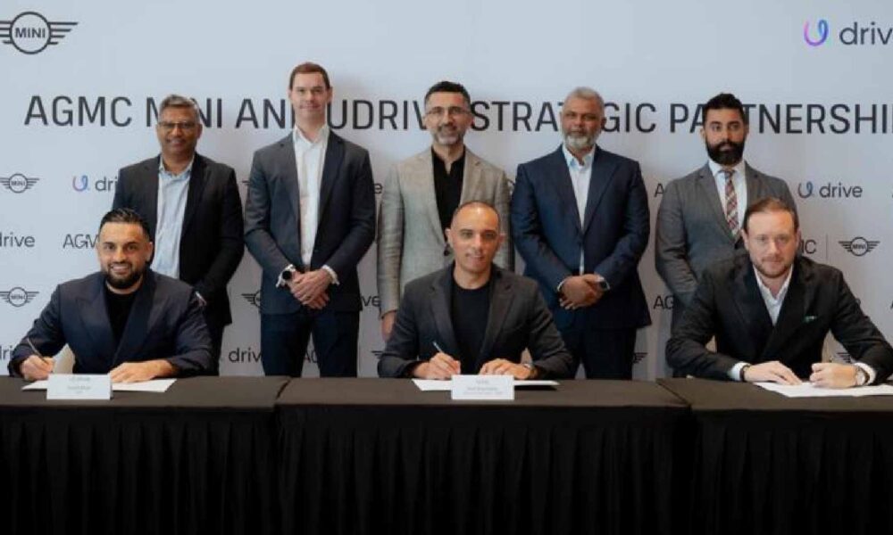 Udrive and AGMC MINI executives sign a strategic partnership agreement during an MoU ceremony, seated at a table with branded backdrop.