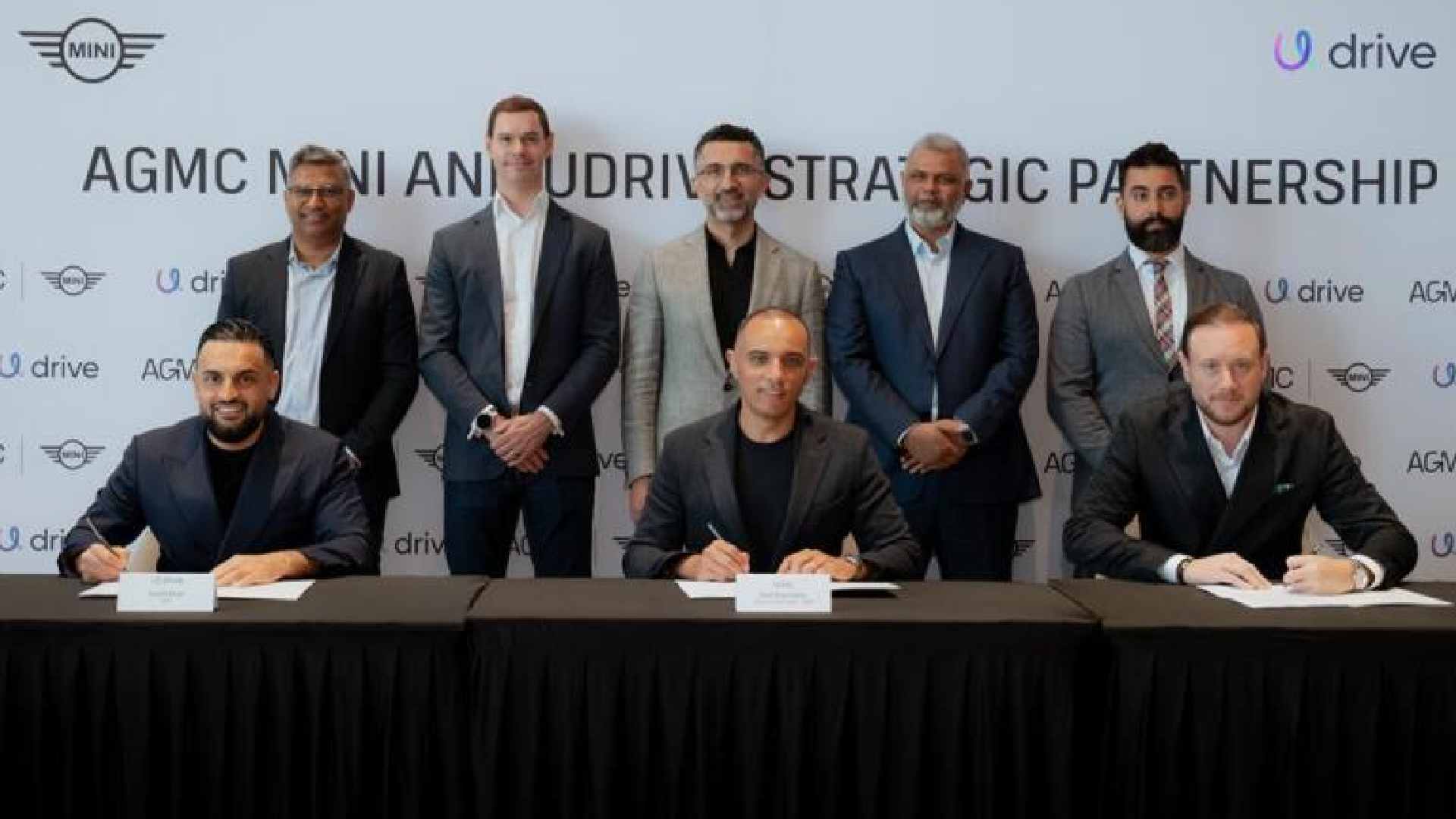 Udrive and AGMC MINI executives sign a strategic partnership agreement during an MoU ceremony, seated at a table with branded backdrop.