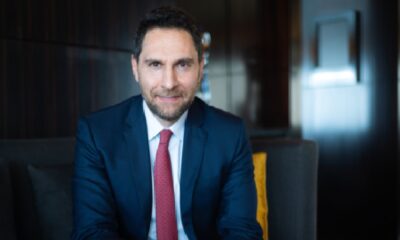 Executive from IHG Hotels & Resorts seated indoors on a sofa, wearing a navy business suit and red tie, photographed in a modern hotel lounge setting.