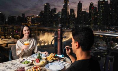 Couple dining at Blume on an outdoor terrace, sharing dessert and drinks with Dubai skyline and waterfront fountain views at night.