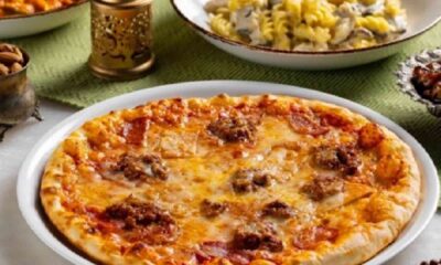 Table spread of dishes at The Big Chill Café featuring a cheese pizza in the foreground, plates of creamy pasta, saffron rice, stir‑fried noodles, and flatbread, arranged with decorative lanterns in a warm café setting